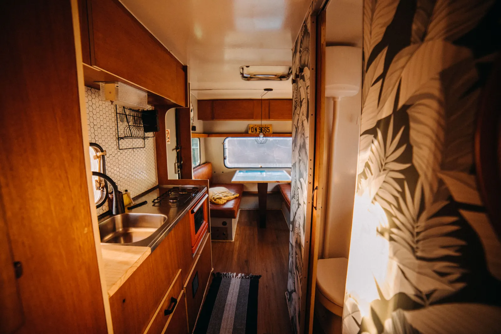 Inside a small camper: a two-burner gas stove and sink along one wall, a dinette at the far end