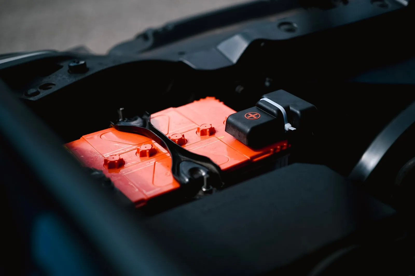 A lead acid battery clamped into a vehicle engine bay, terminals covered