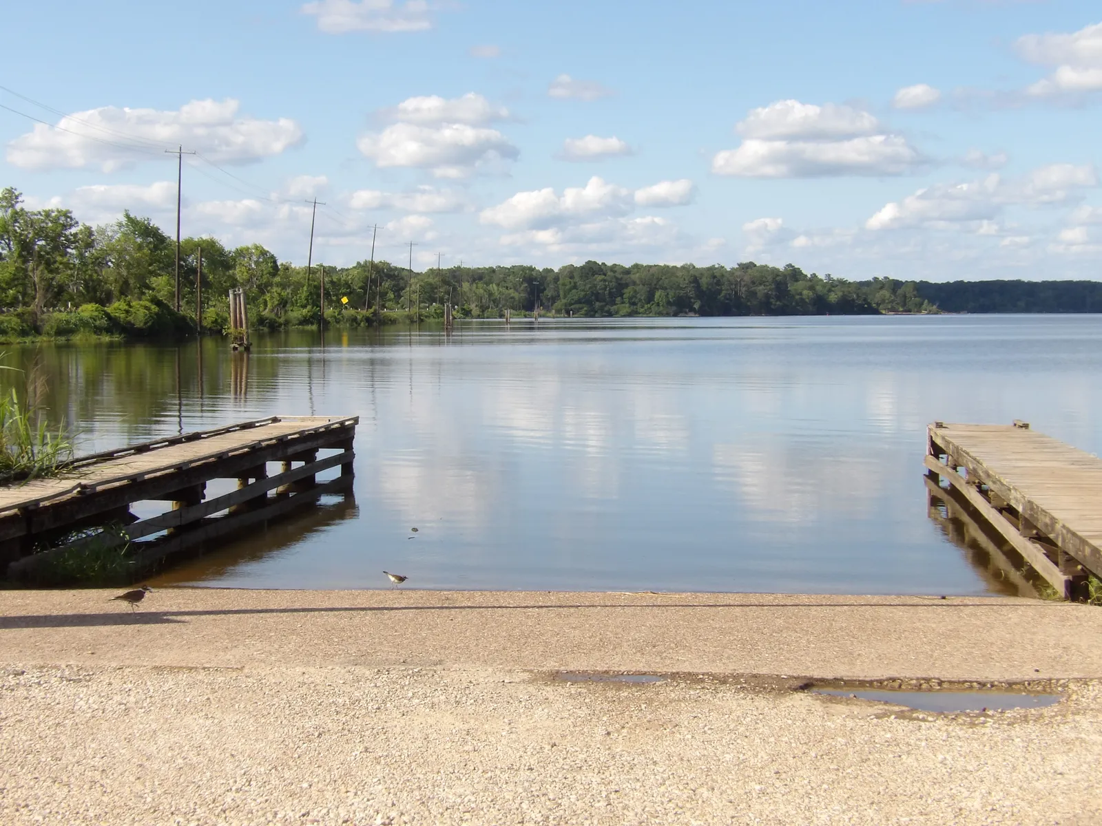 A concrete boat ramp and two wooden docks at a quiet lake under a blue sky