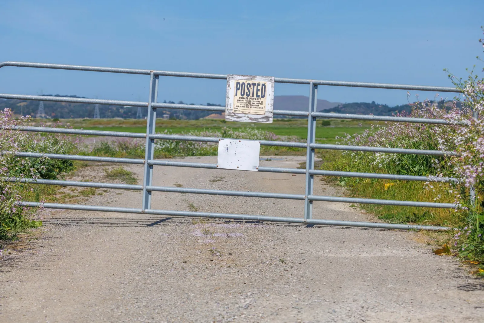 A metal gate closed across a dirt road with a posted private property sign