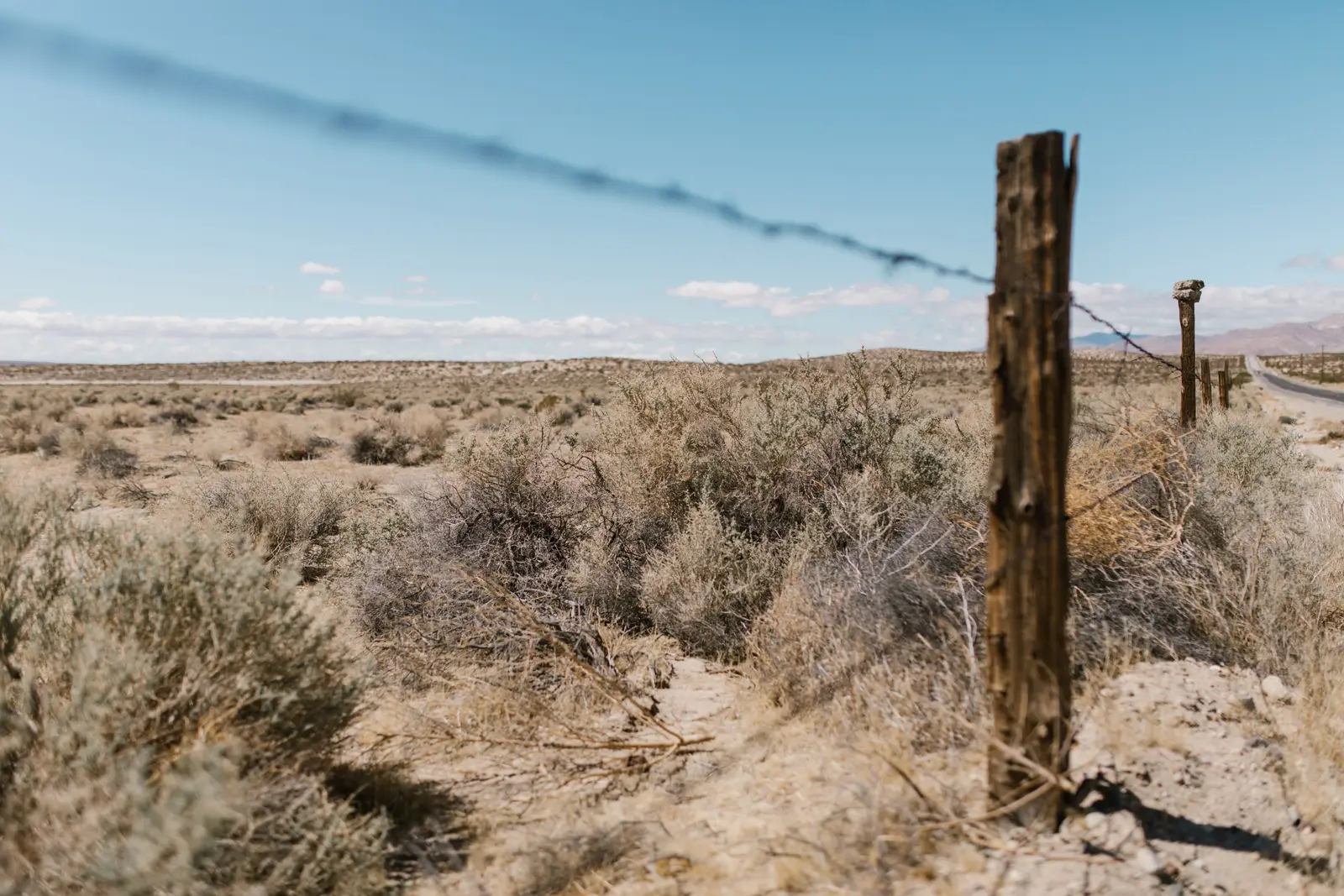 A barbed wire fence line running through dry sagebrush toward a distant road