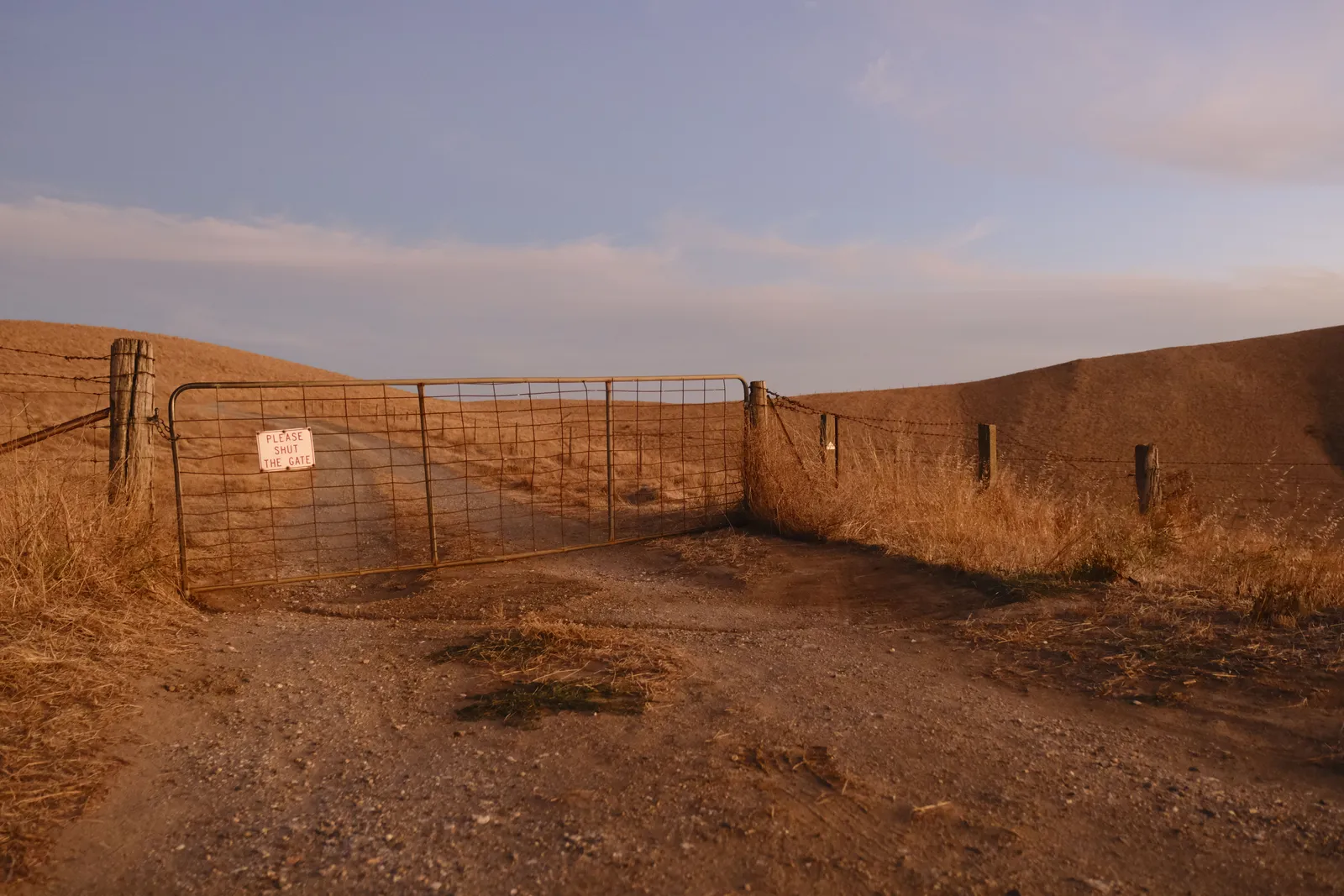 A closed wire gate across a dirt two-track in dry open range country at sunset