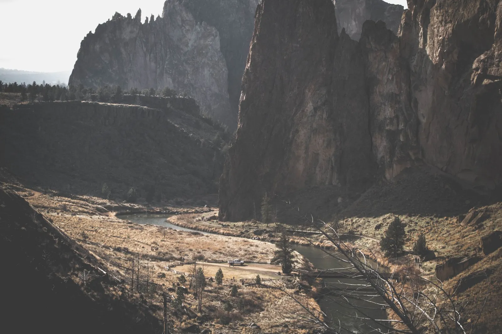 A river winding through a dry canyon below rimrock cliffs, with yellow grass and scattered junipers