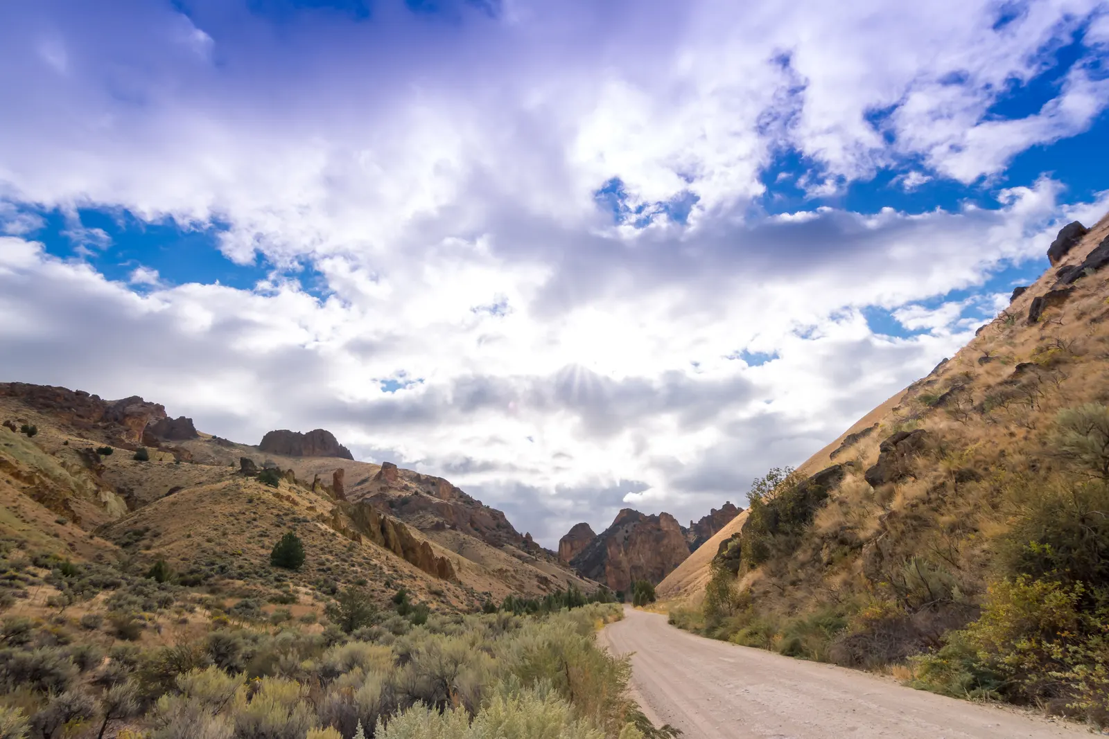 A gravel road running through dry sagebrush hills and rock outcrops in high desert country