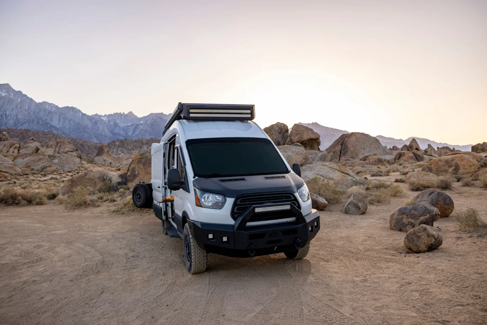 Camper van parked alone on a dirt pad in rocky desert country at dusk