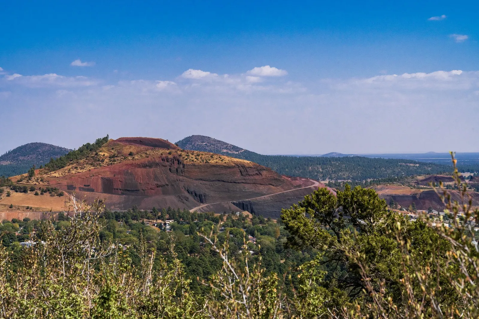 A red cinder cone rising above pine forest under a clear sky near Flagstaff, Arizona