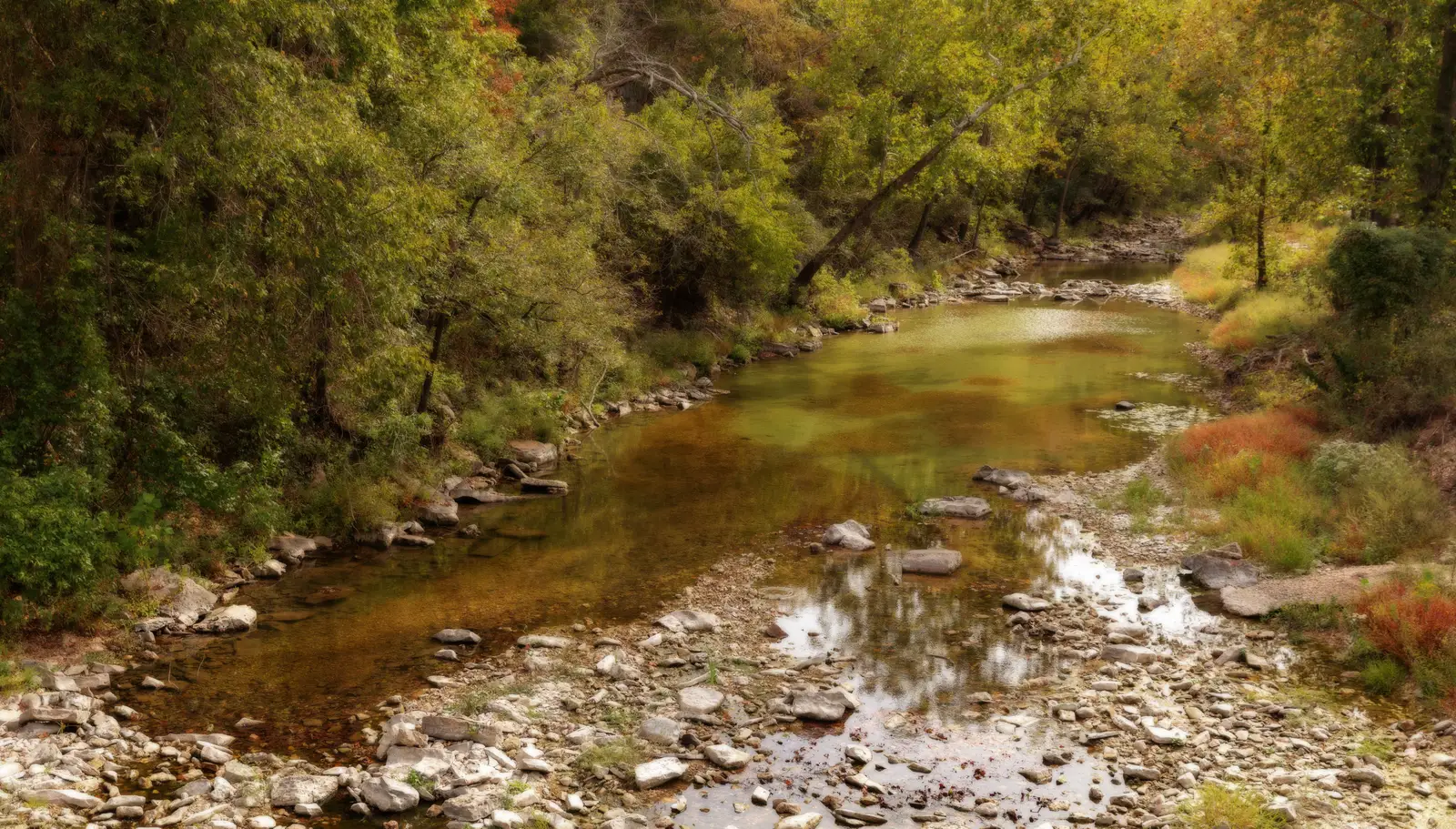 A shallow, rocky creek with gravel banks running through an Arkansas forest in early autumn