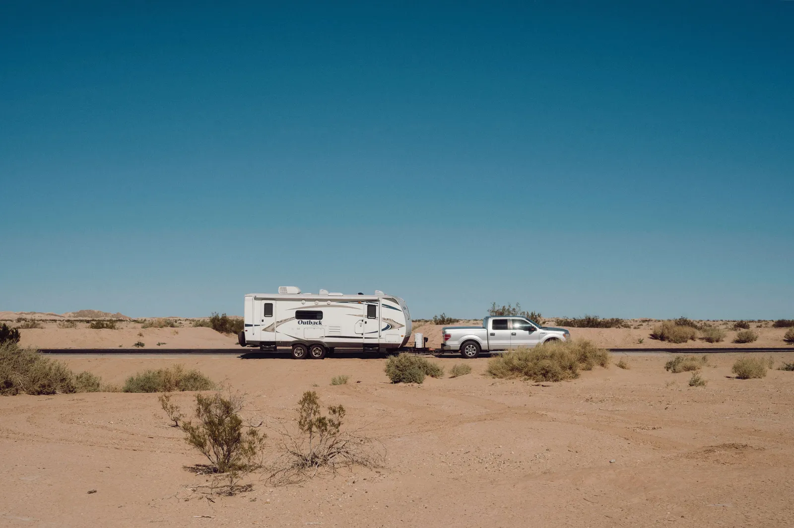 A pickup truck towing a travel trailer along a desert highway under a clear sky