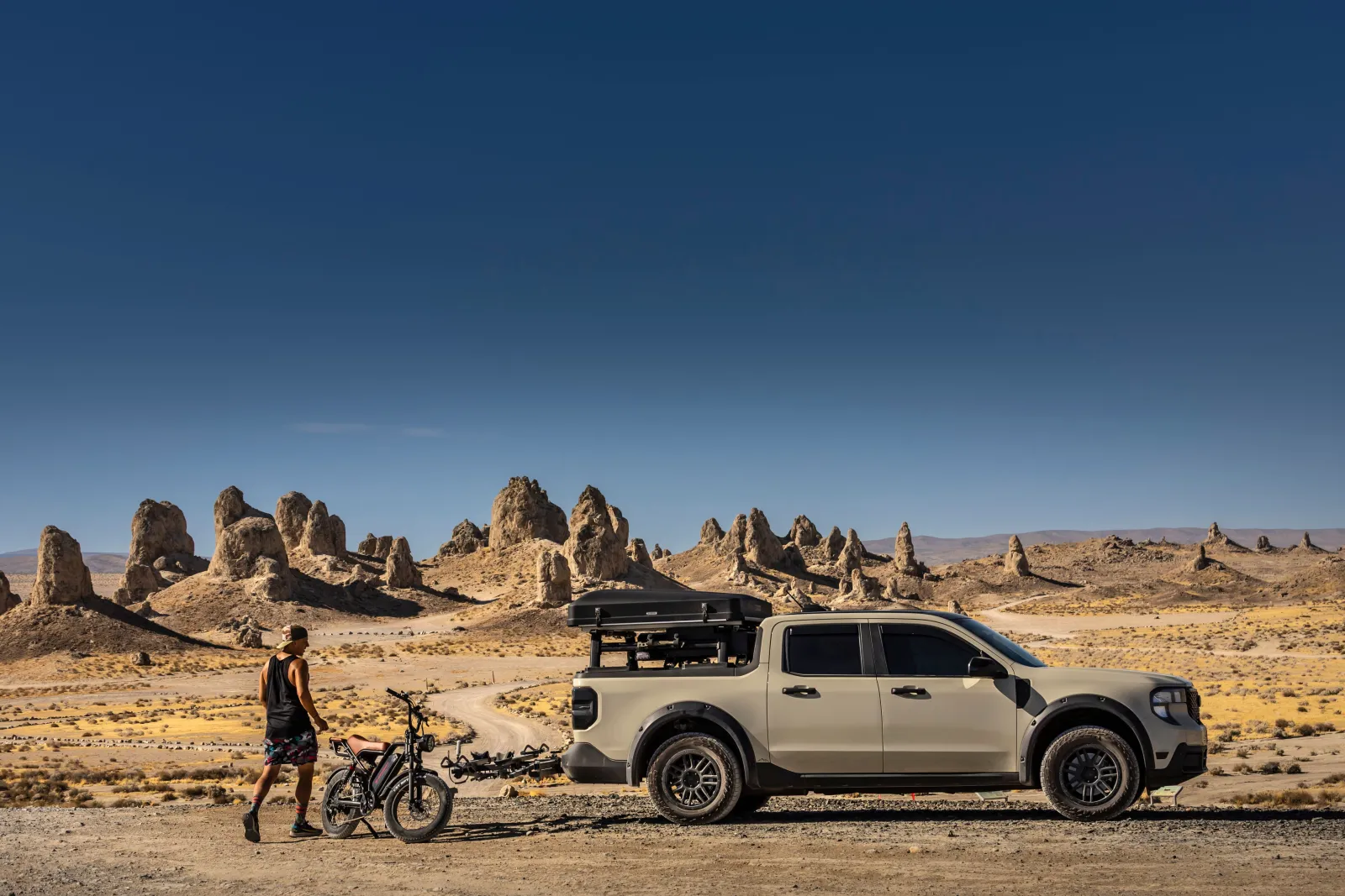 A pickup truck and a person with an electric bike on open desert ground at Trona Pinnacles, California, under a clear sky