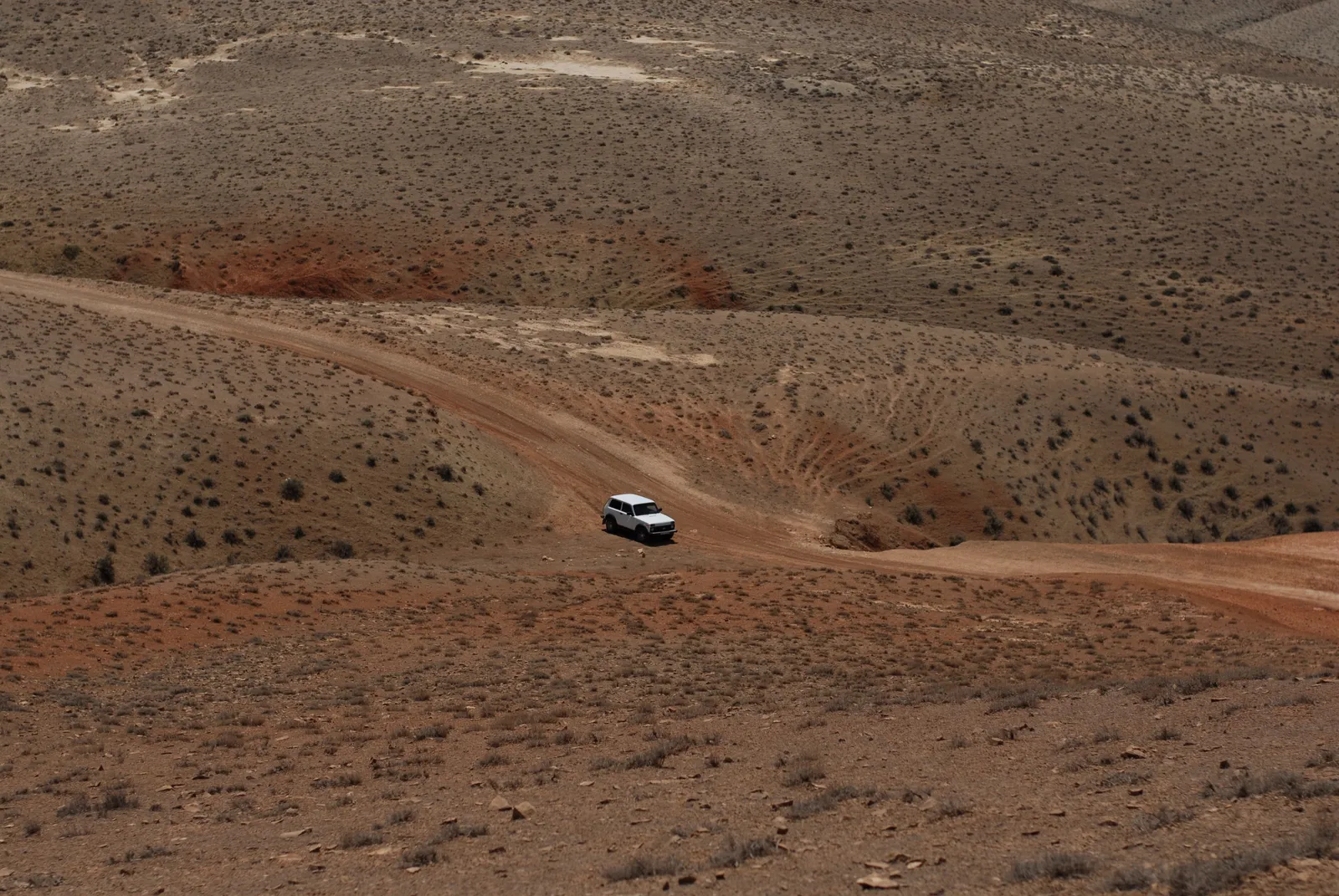A single high clearance vehicle on a graded dirt road crossing empty desert hills