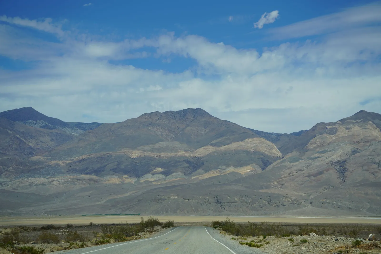 An empty two-lane road running toward the bare desert mountains of Death Valley