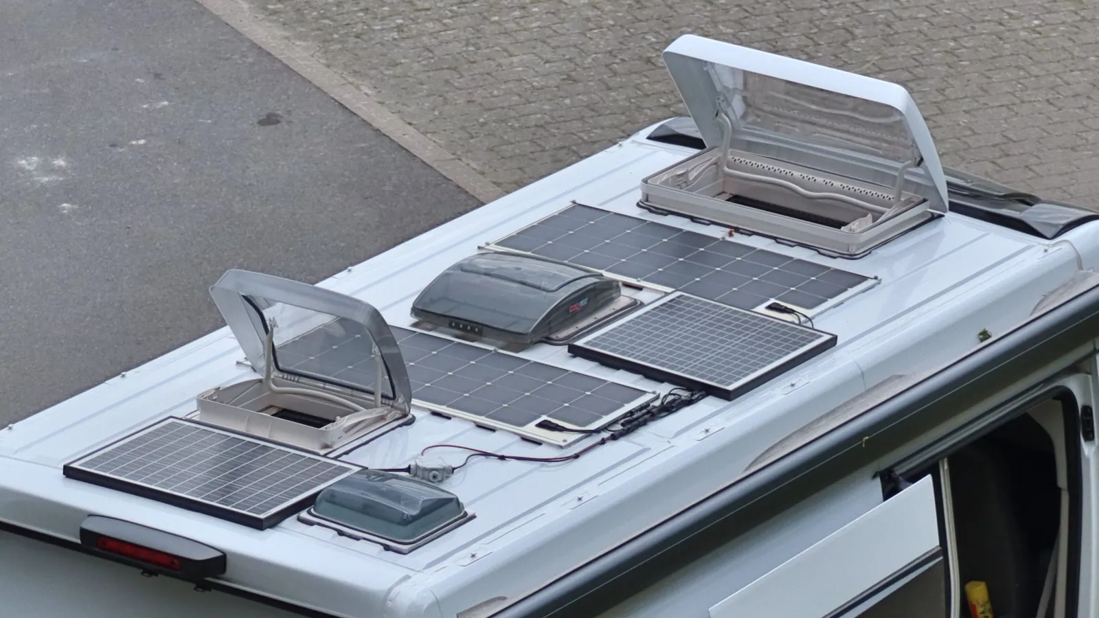 Several solar panels mounted flat on the roof of a white camper van, seen from above