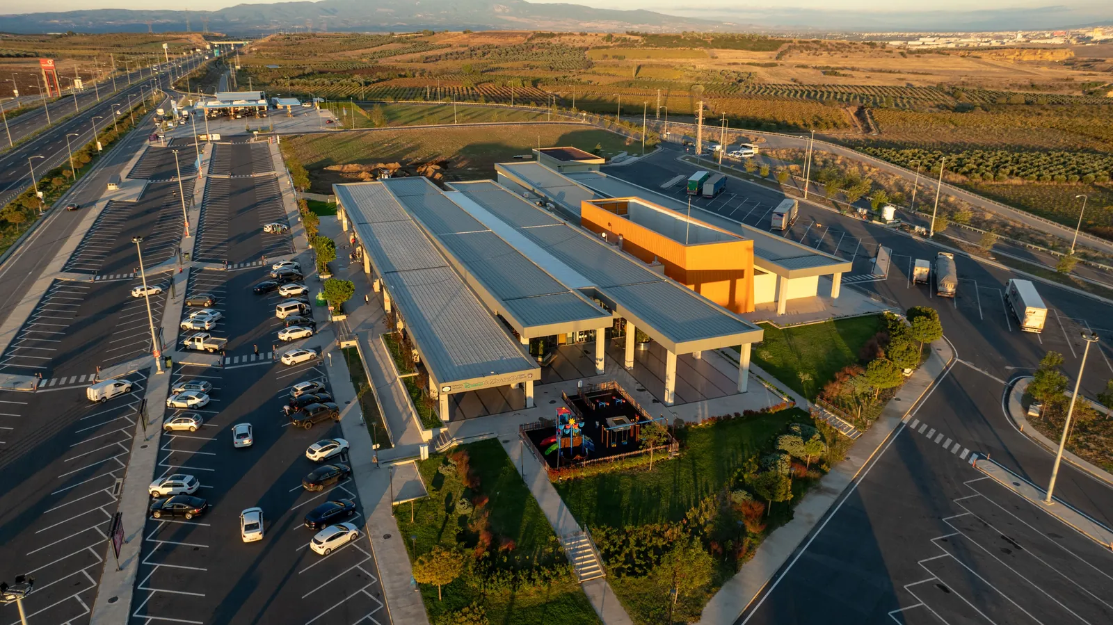 An aerial view of a highway rest area and its parking bays at sunset