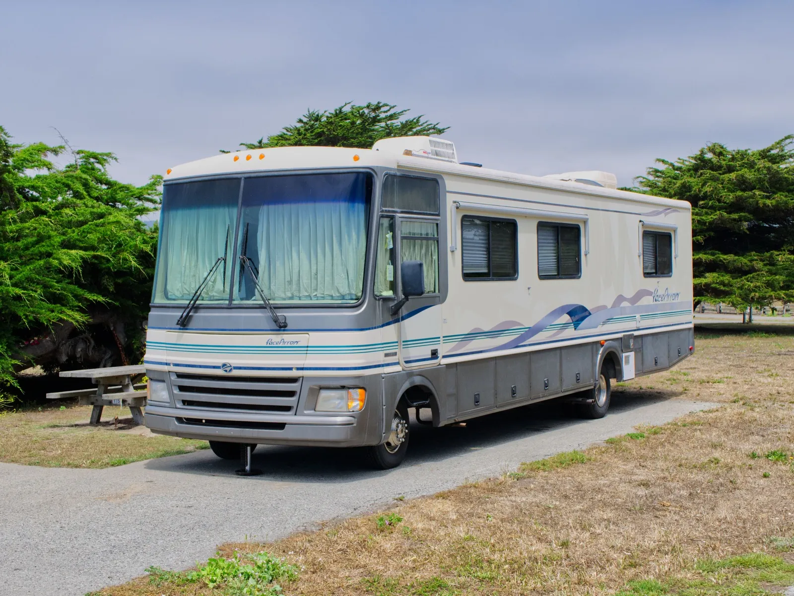 A Class A motorhome parked on a paved campground pad beside a numbered picnic table