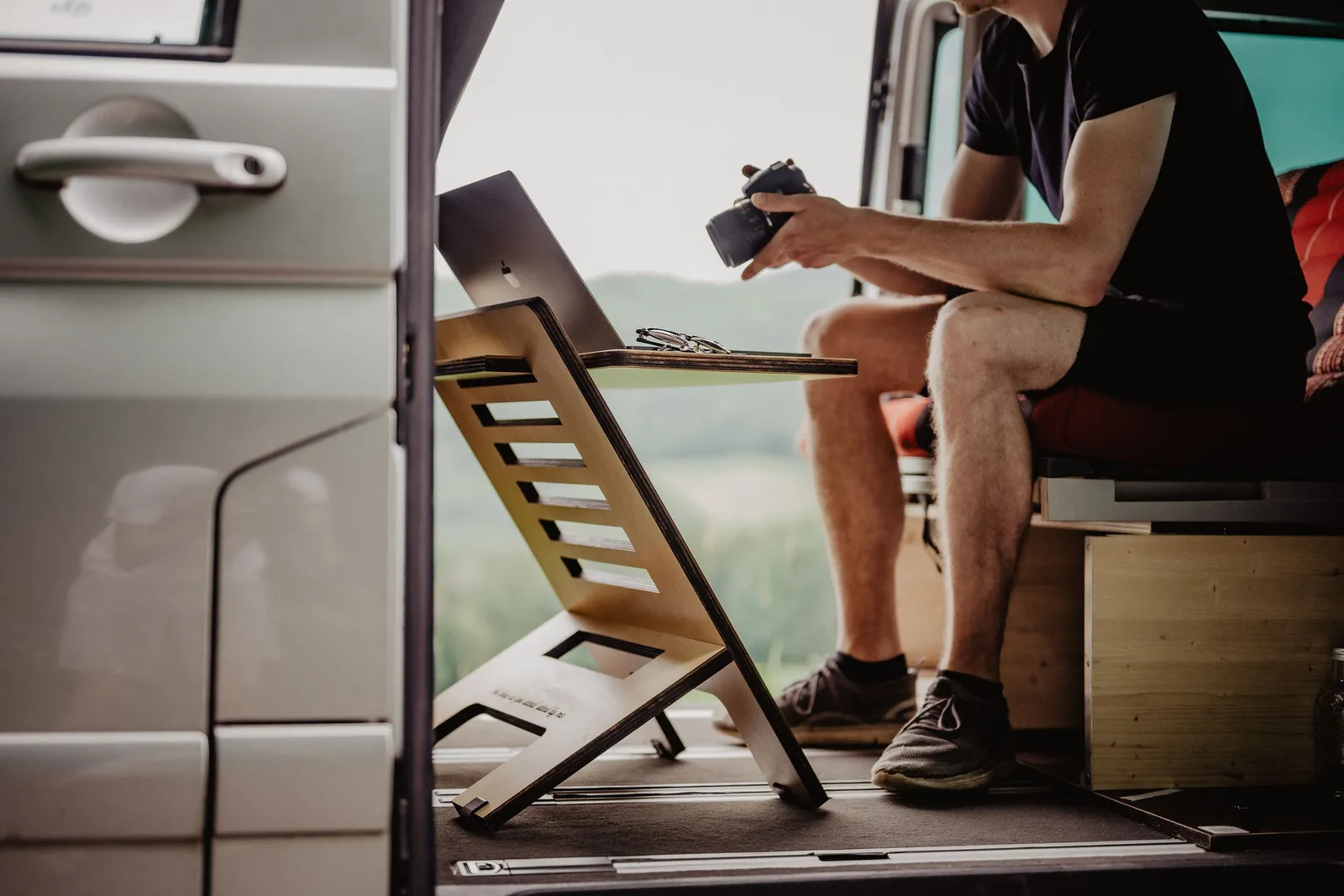 A laptop on a wooden stand in the open side door of a parked camper van