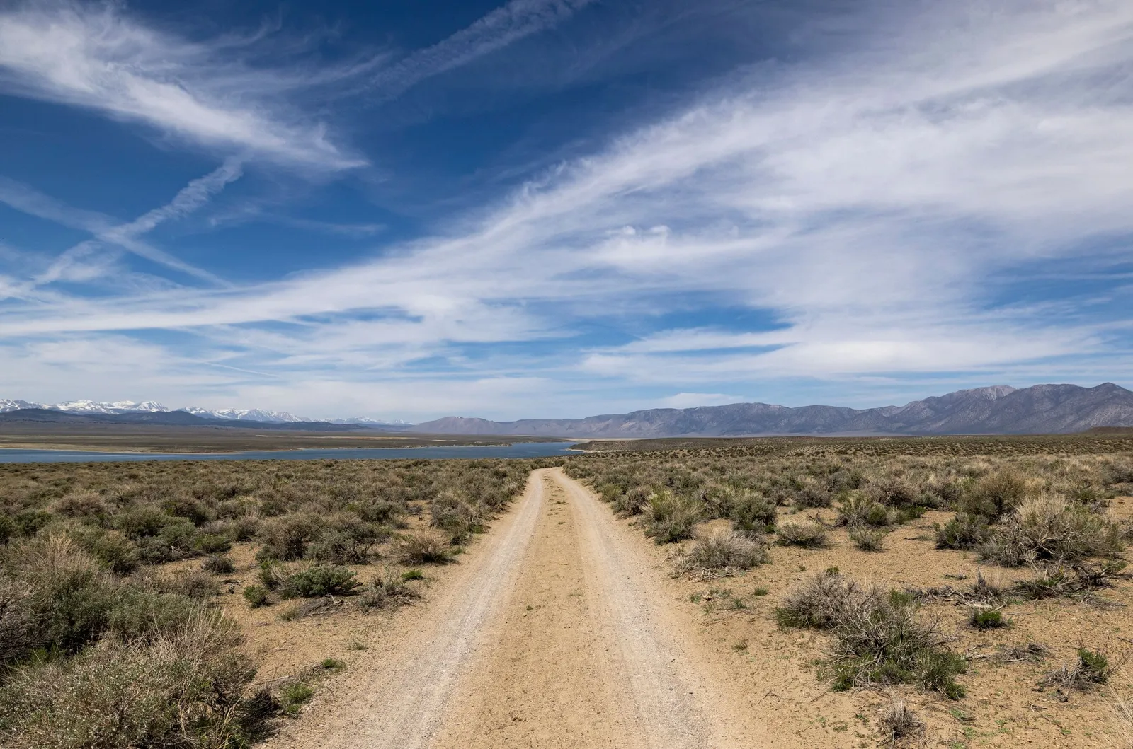 A dirt road running through open desert toward distant snowy mountains