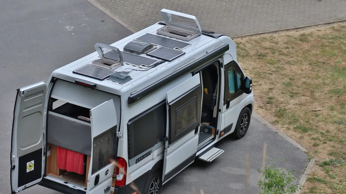 A camper van with solar panels on the roof and its side and rear doors open
