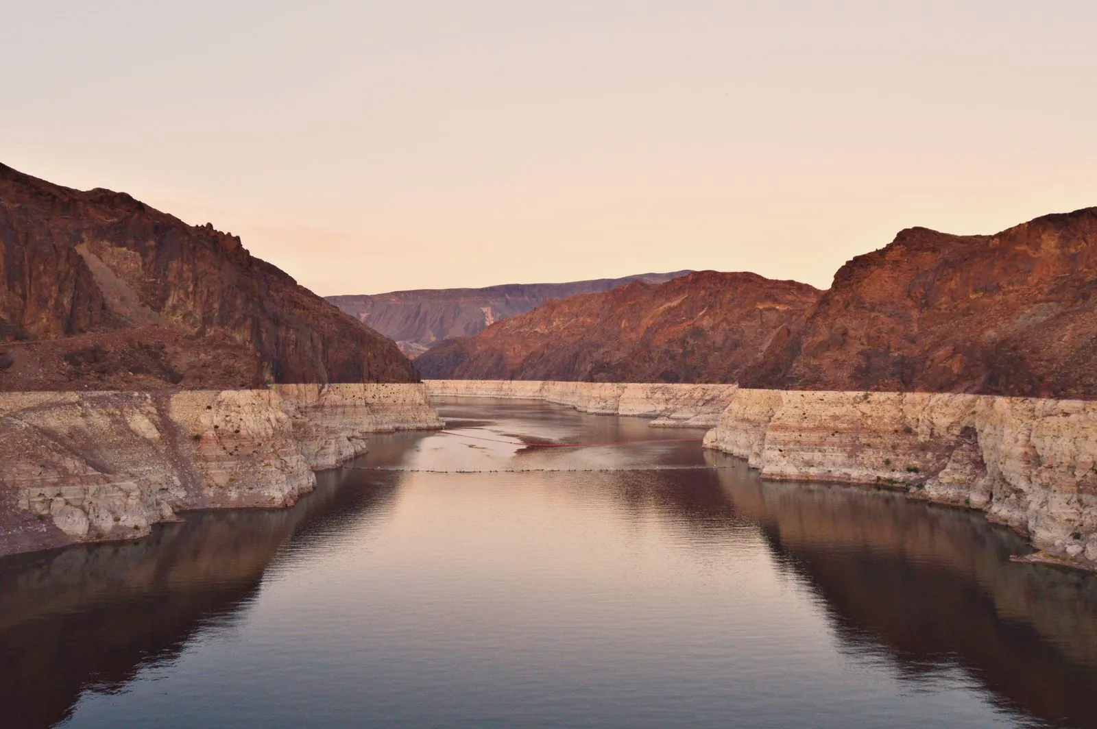 A desert canyon reservoir with a pale mineral ring along its rock walls at sunset