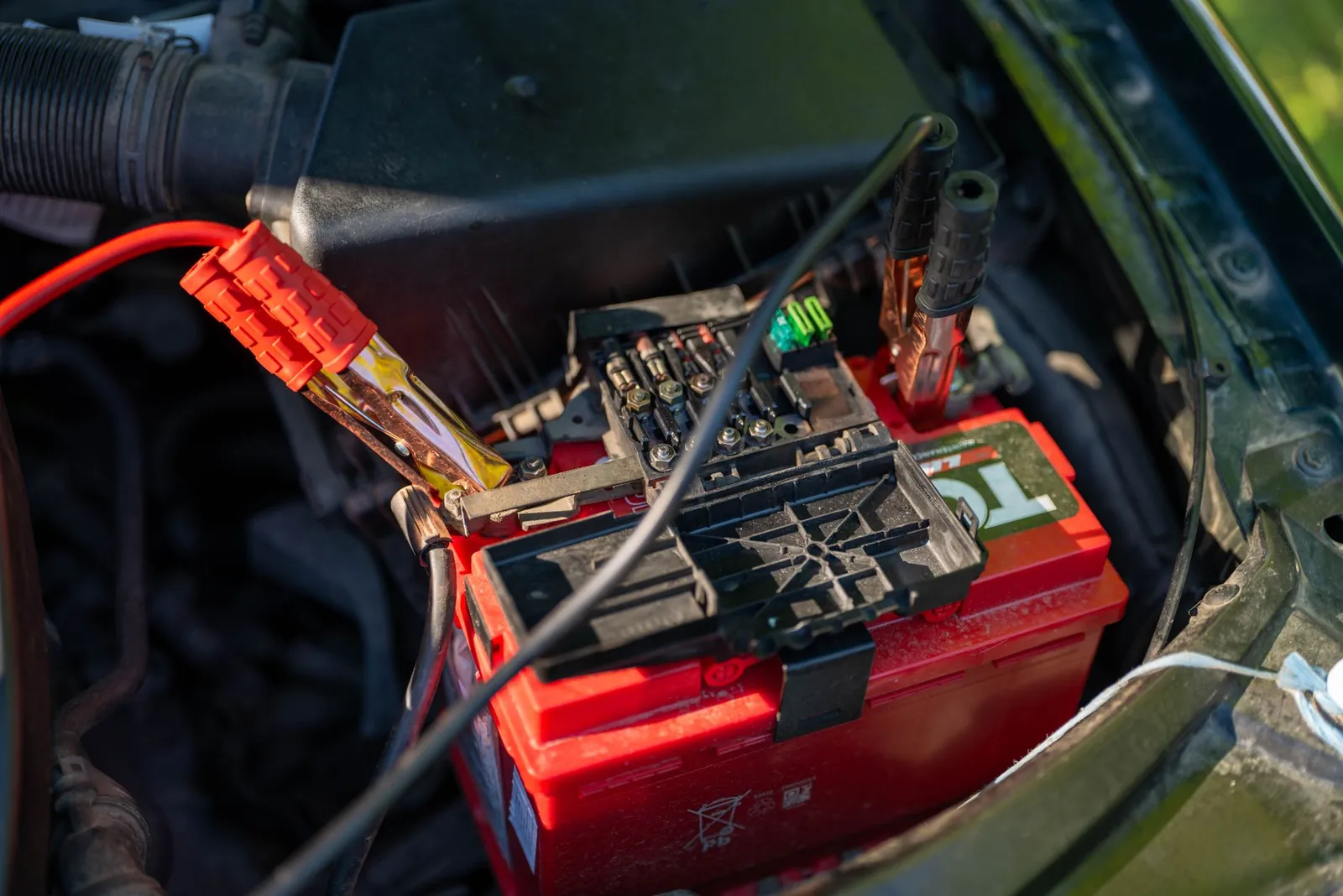 Clamps landed on the terminals of a red lead acid battery in a vehicle engine bay