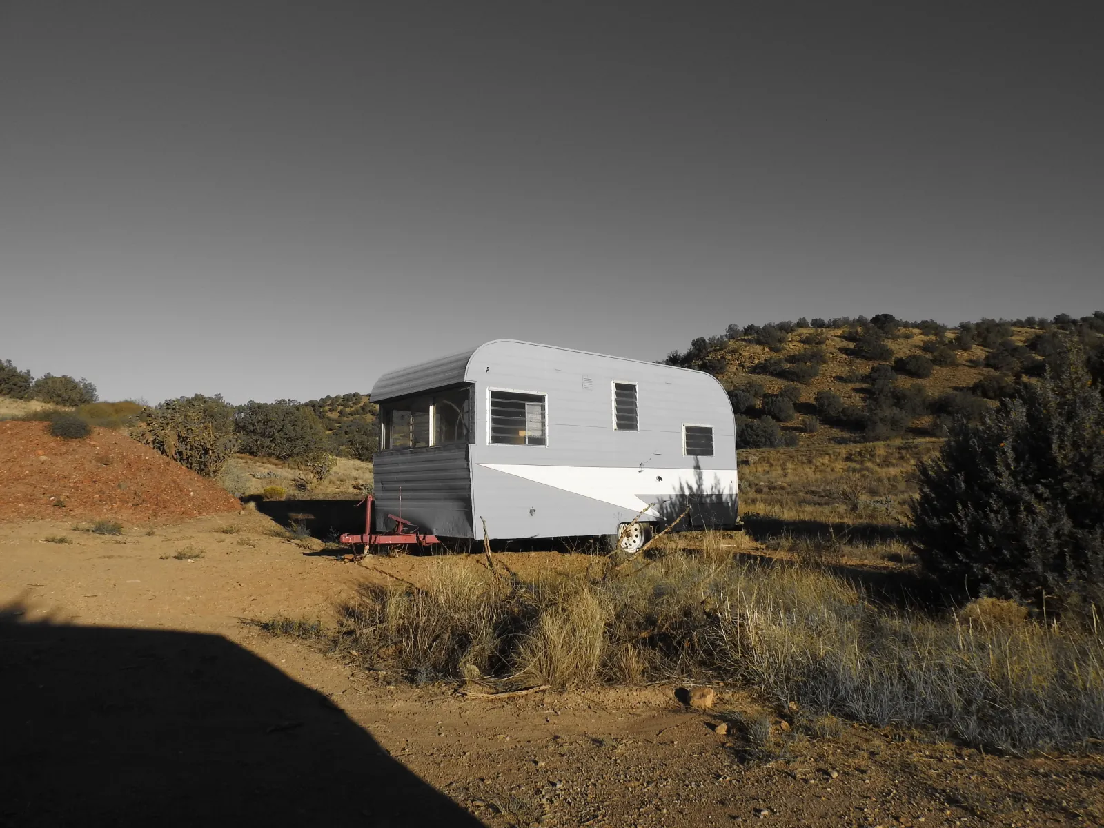 A small vintage travel trailer parked on dirt among desert scrub