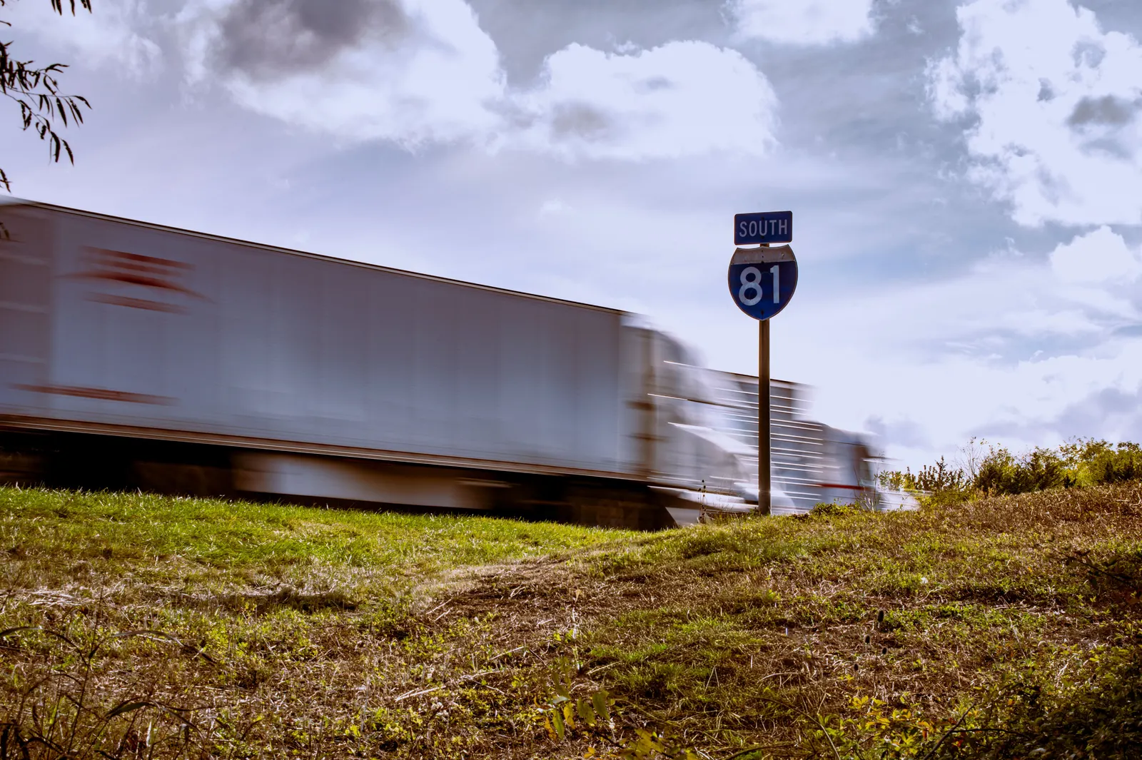Semi truck passing an Interstate 81 South route marker on a grassy highway shoulder