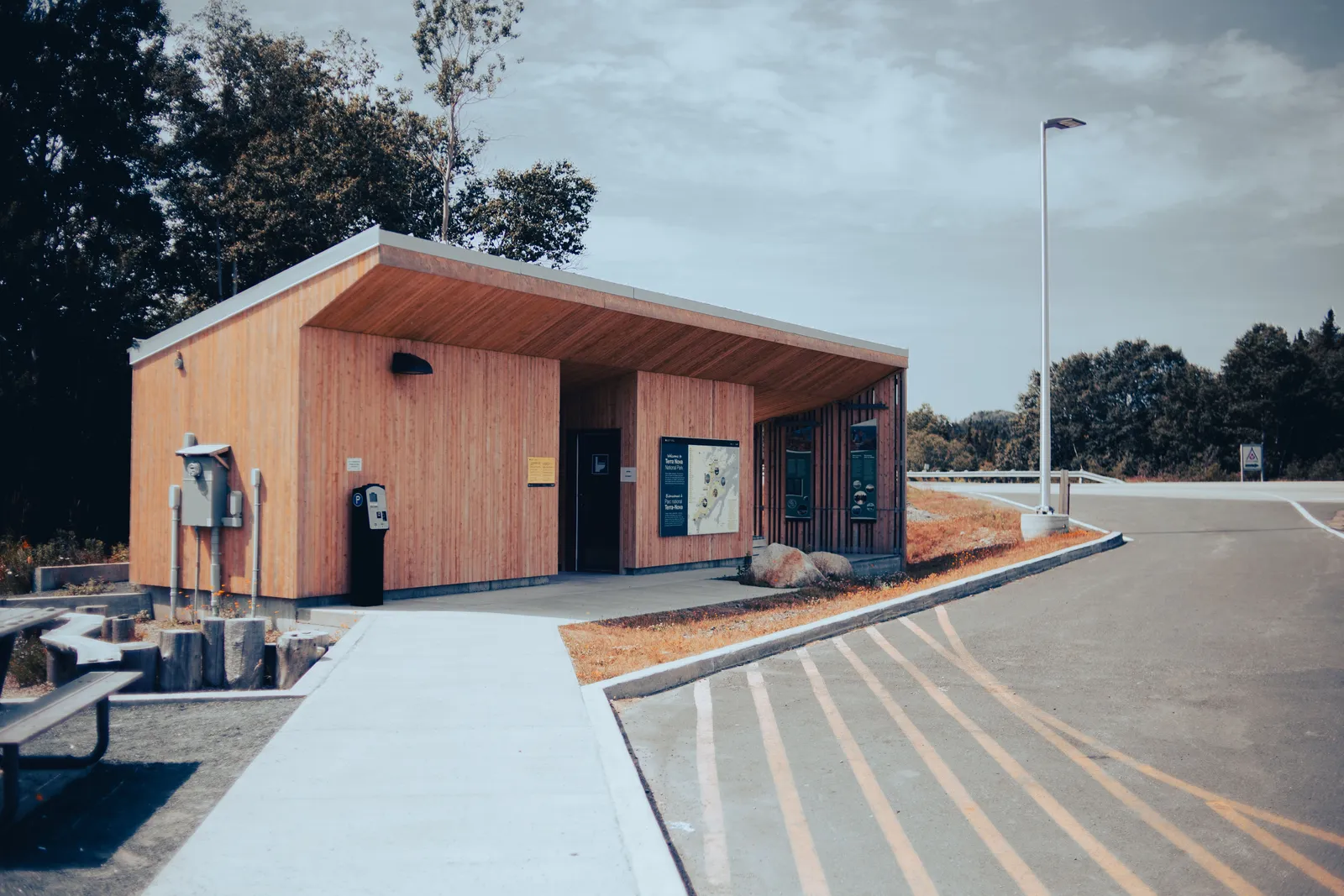 An empty roadside rest area with a wooden restroom building, a picnic table and striped parking