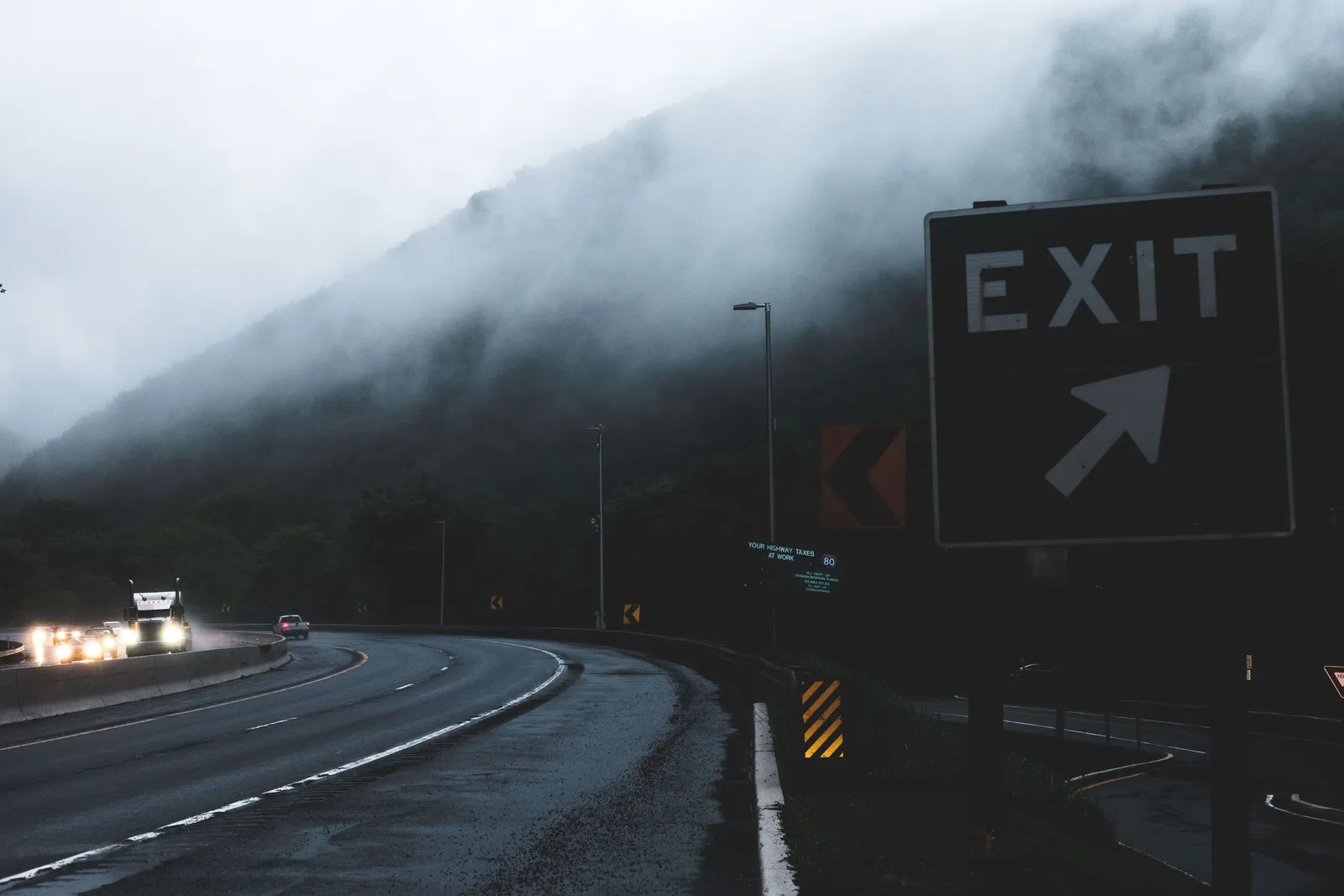 Highway exit sign in fog at twilight with vehicles on the road below