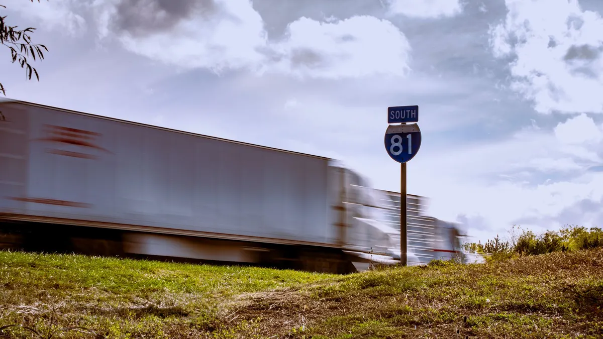 A semi truck passing an Interstate 81 South route marker on a grassy roadside