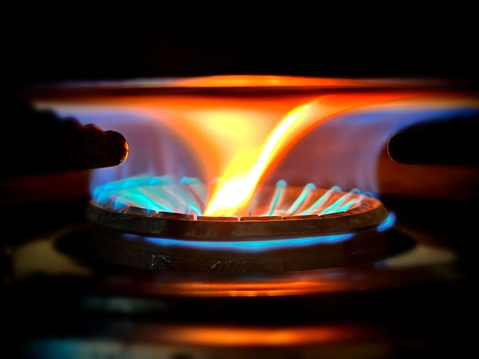 A gas burner flame, blue at the ring and orange at the tips, against a dark background