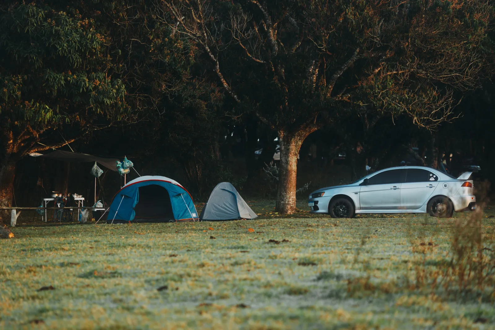 Two tents pitched at a grassy campsite with a sedan parked alongside them