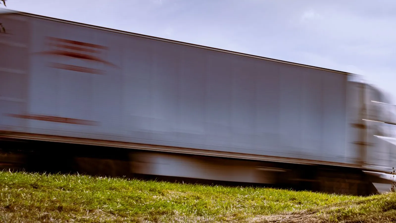 A tractor trailer passing at speed, seen from the grass shoulder of an interstate