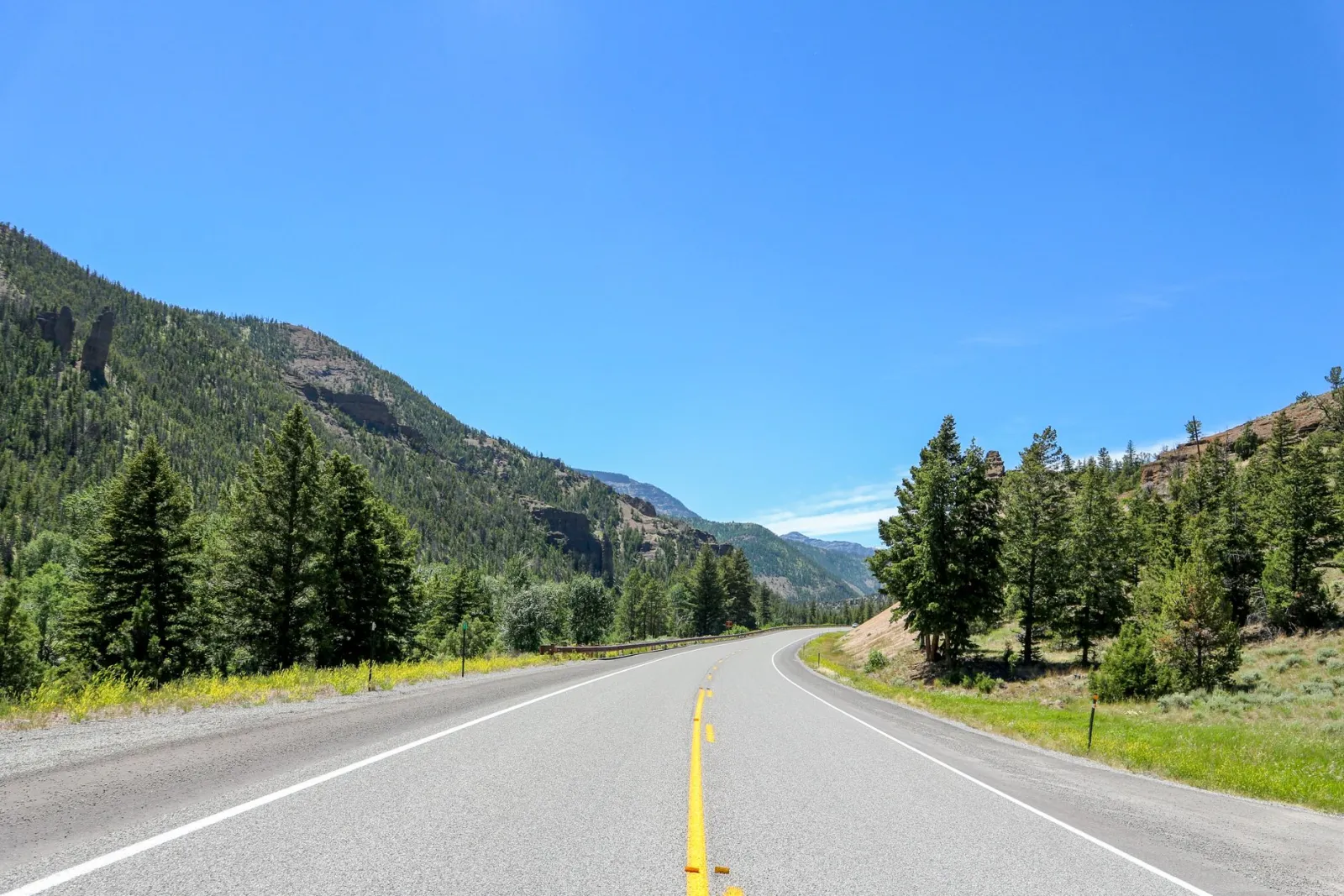 An empty two lane road curving through open sagebrush country toward snow dusted mountains
