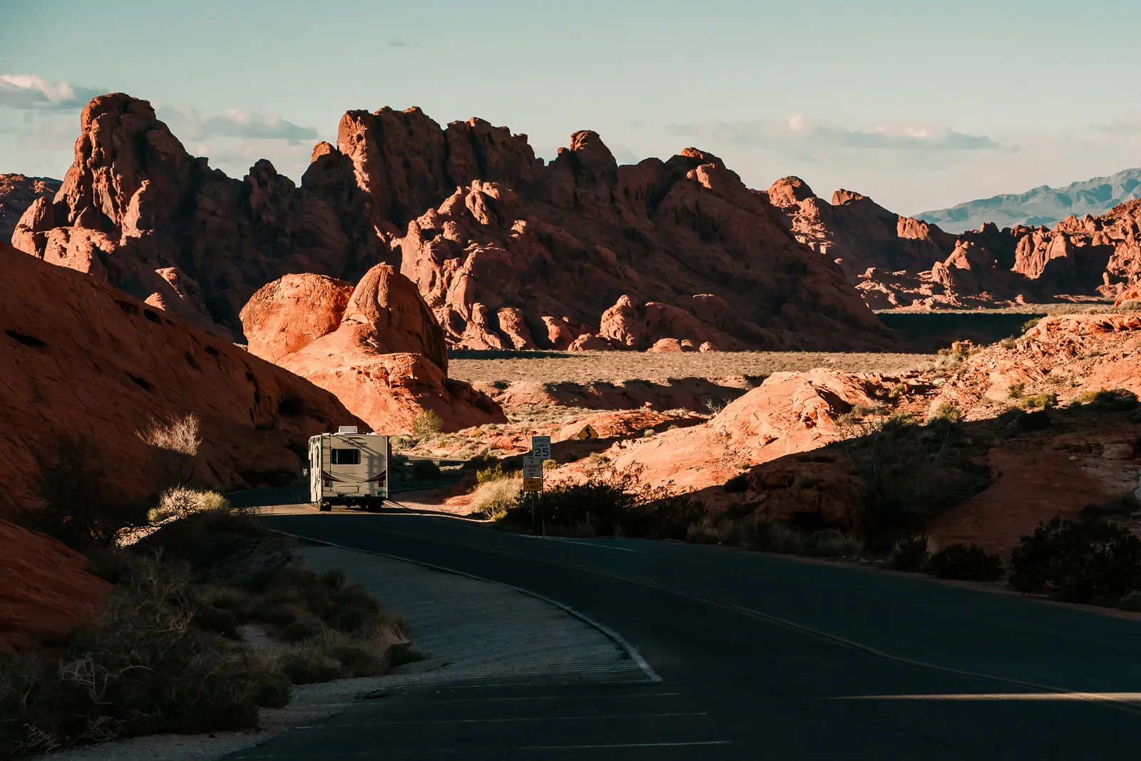 A motorhome on a narrow two lane road through red rock desert, with a 25 mph speed limit sign ahead